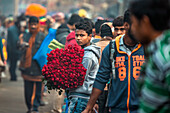Kolkata, India - 28 January 2023: View of a young man amidst a bustling crowd, holding a vibrant bouquet of red roses, a splash of color against the muted background.