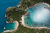 Aerial view of turquoise waters embracing the rocky coastline and lush green vegetation of Corfu's hidden beaches, Corfu, Corfu, Greece.