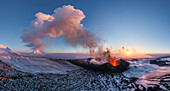 Luftaufnahme von feuriger Lava, die aus einem Vulkan ausbricht, im Kontrast zur schneebedeckten Landschaft unter einem pastellfarbenen Himmel, Kamtschatka, Russland.