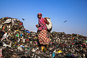 Chittagong, Bangladesch - 08. März 2024: Blick auf eine Frau in leuchtendem Rot inmitten einer ausgedehnten Landschaft aus weggeworfenem Müll unter einem klaren blauen Himmel.
