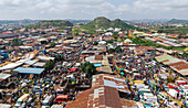 Aerial view of a sprawling market teeming with vibrant activity and bustling crowds beneath the gaze of distant rocky hills, Jos, Plateau, Nigeria.