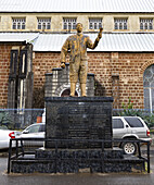 Freetown, Sierra Leone - 11. August 2021: Ansicht der Statue mit erhobener Hand vor dem Hintergrund eines Gebäudes, wobei sich das dunkle Denkmal von der hellen Struktur abhebt.