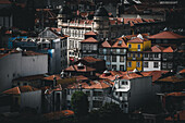 Porto, Portugal - 17. Juni 2022: Blick auf Terrakotta-Dächer, die kaskadenartig den Hang hinunterfallen, unterbrochen von leuchtend gelben und blauen Fassaden vor einem Hintergrund von Kuppelbauten.