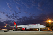 Nairobi, Kenya - 26 August 2014: View of a Kenya Airways Embraer jet bathed in the soft glow of twilight beneath a sky streaked with wispy clouds.