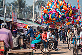 Bogura, Bangladesh - 03 November 2023: View of a vibrant street scene with a rickshaw carrying passengers and a burst of colorful balloons against the backdrop of market stalls.