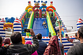 Bogura, Bangladesh - 03 November 2023: View of children gleefully sliding down an inflatable slide, while onlookers capture the moment with their phones, creating a vibrant scene of joy and festivity.