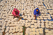 Bogura, Bangladesh - 24 April 2021: View of women in vibrant saris meticulously arranging seemingly endless rows of sun-bleached food under the warm sky.