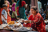 Bogura, Bangladesh - 03 November 2023: View of a woman in a vibrant red sari amidst the bustling marketplace, surrounded by piles of sweets and savory snacks.