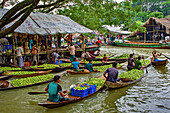 Swarupkathi, Bangladesh - 28 July 2017: View of boats laden with vibrant green produce jostling along the waterway near market stalls, a lively scene of trade and rural life.