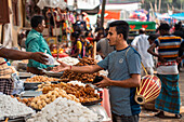 Bogura, Bangladesh - 03 November 2023: View of a busy market scene with a vendor offering sweets, the vibrant colors of the local products contrasting with the earthy tones of the surroundings.