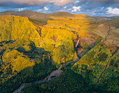 Aerial view of cascading waterfalls slicing through sun-kissed cliffs blanketed in vibrant green vegetation, a serene landscape of natural beauty, Fajãzinha, Azores, Portugal.