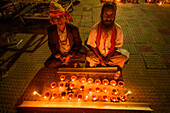 Narayanganj, Bangladesh - 11 June 2018: View of two men seated on the ground, surrounded by an array of flickering diyas, their gentle light casting warm glows on the patterned tiles.