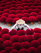 Aerial view of bright crimson incense sticks drying under the sun, creating a vivid contrast against the worker's attire, Quang Phu Cau, Hanoi, Vietnam.