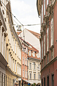 View of colorful buildings lining a narrow street, with intricate architectural details and overhead wires creating a sense of depth, Graz, Austria.