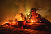 Narayanganj, Bangladesh - 11 June 2018: View of people lighting diyas casting an ethereal glow, as smoke swirls, creating a mystical atmosphere.
