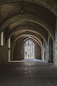 View of stone arches casting long shadows, leading to a brightly lit opening in an ancient building, a timeless scene of architectural beauty, Gubbio, Umbria, Italy.