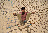 Bogura, Bangladesh - 23 March 2023: View of a man holding up thin, sun-dried noodles amidst a vast expanse of drying pasta, creating a textural tapestry under the open sky.