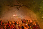 Narayanganj, Bangladesh - 11 June 2018: View of a gathering amidst a smoky atmosphere, with a brightly lit temple structure in the background, contrasting with the dark tree silhouette.