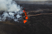Luftaufnahme von geschmolzener Lava, die sich durch die dunkle Vulkanlandschaft schlängelt, ein feuriger Fluss im Kontrast zum kühlen, ätherischen Rauch, Grindavik, Region Südliche Halbinsel, Island.