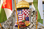 View of the Hungarian coat of arms framed by vibrant national flags and topped with the Holy Crown, a symbol of history, Budapest, Hungary.