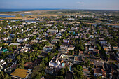 Aerial view of a dense tapestry of buildings and lush greenery blending towards the coast, with a serene blue sky above, Karaikal, Puducherry, India.
