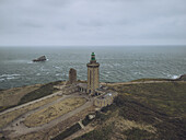 Aerial view of the majestic Cap Fréhel lighthouse standing tall against the turbulent sea, with the rugged coastline adding drama to the scene, Plévenon, Bretagne, France.