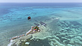 Aerial view of a tiny island with a red-roofed structure surrounded by shallow turquoise waters and distant dark rocks, San Andrés, San Andres and Providencia, Colombia.