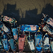 Luftaufnahme einer Flotte von Fischerbooten, ein lebhafter Wandteppich aus Blau-, Rot- und Grüntönen, die dicht beieinander liegen und lange Schatten auf das Wasser werfen, Yanam, Puducherry, Indien.
