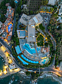 Aerial view of the luxurious resort with its pools reflecting the twilight sky, nestled between the coastline and winding roads, a beacon of relaxation, Chania, Chania, Greece.