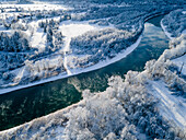 Aerial view of a meandering river cutting through a snow-laden forest, the white trees contrasting with the turquoise water, Füssen, Bavaria, Germany.