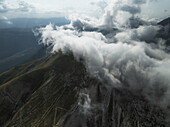 Luftaufnahme der zerklüfteten, felsigen Gipfel des Gran Sasso, eingehüllt in himmlische Wolken, ein Tanz von Licht und Schatten über der Landschaft, Gran Sasso, Abruzzen, Italien.