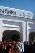 Kartarpur, Pakistan - 09. November 2019: Blick auf Pilger in leuchtenden Orange- und Blautönen, die sich am Eingang des Darshan Deori versammeln, umrahmt von seiner strahlend weißen Fassade.