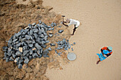 Mahabalipuram, India - 16 September 2006: Aerial view of workers in the sand, one breaking rocks with a hammer, the other watching, a contrast of labor and stillness.