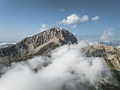 Luftaufnahme des majestätischen Gran Sasso, der durch ein Meer wirbelnder Wolken hindurchragt, gebadet in das sanfte Licht der italienischen Sonne, Gran Sasso, Abruzzen, Italien.