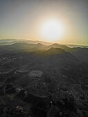 Aerial view of sun-kissed peaks and valleys blend in a hazy embrace, casting long shadows over the rugged landscape, Aaqoura, Mount Lebanon Governorate, Lebanon.