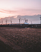 Fujiokaminami, Japan - 02 March 2025: View of a high-speed train slicing through the landscape beneath a pastel sky, its sleek form a blur against the muted earth tones.