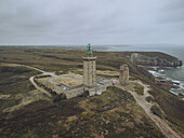 Aerial view of Phare du Cap Fréhel lighthouse stands tall against the rugged coastline, where the emerald sea meets the ochre cliffs, Plévenon, Bretagne, France.