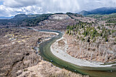 Aerial view of the Stillaguamish River snaking through a landscape of bare trees and rugged mountains, with a cloudy sky above, Arlington, Washington, United States.