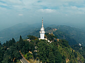Aerial view of the white Ambuluwawa Tower piercing the sky above verdant hills, a beacon amidst the serene landscape, Ambuluwawa Tower, Central Province, Sri Lanka.