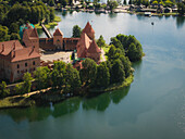 Luftaufnahme der mittelalterlichen Burg auf der Insel Trakai: Die roten Ziegelsteine bilden einen atemberaubenden Kontrast zu den üppig grünen Bäumen und dem ruhigen Wasser des Sees, Trakai, Litauen.