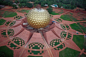 Luftaufnahme der ikonischen Matrimandir-Struktur, eine goldene Kugel, die sich von dem roten Backsteinsockel und den geometrischen Mustern abhebt und ein faszinierendes Schauspiel bietet, Bommayapalayam, Tamil Nadu, Indien.
