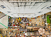 Luftaufnahme eines belebten Marktplatzes, auf dem es vor Menschen wimmelt, im Schatten eines hohen Gebäudes, eine lebendige Szene von Handel und Gemeinschaft, Buguma, Rivers State, Nigeria.