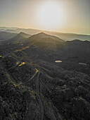 Aerial view of the rugged, mountainous terrain bathed in the warm glow of the setting sun, casting long shadows across the landscape, Aaqoura, Mount Lebanon Governorate, Lebanon.