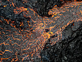 Luftaufnahme von Flüssen aus geschmolzener Lava, die sich durch gehärtetes schwarzes Vulkangestein schlängeln und einen starken Kontrast aus Feuer und Stein bilden, Grindavik, Grindav?kurb?r, Island.