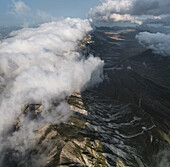 Luftaufnahme von Wolken, die sich an die zerklüftete Hochebene des Campo Imperatore klammern und Schatten über die dramatische Landschaft des Gran Sasso, Abruzzen, Italien, werfen.