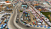 Luftaufnahme des Isaac Boro Park, der mit Autos und Händlern unter bunten Sonnenschirmen belebt ist, ein pulsierender Knotenpunkt von Handel und Bewegung, Abali Park, Port Harcourt, Nigeria.