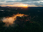 Aerial view of the ancient rock fortress emerging through the mist at sunset, a golden crown amidst the emerald jungle, Lion Rock, Central Province, Sri Lanka.