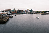 View of a boat sailing on the water with buildings in the background, the scene is bathed in the diffused light of an overcast day, Cardiff, Wales, United Kingdom.