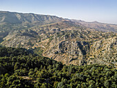 Luftaufnahme von zerklüfteten Bergen, die sich aus einem üppigen Wald erheben, ein Wandteppich aus Grün und Braun unter einem klaren Himmel, Tannourine El Faouqa, Nord-Gouvernorat, Libanon.