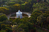 Aerial view of the Aayi Mandapam, a white monument, stands out amidst a sea of green trees under the bright sun, White Town, Puducherry, India.